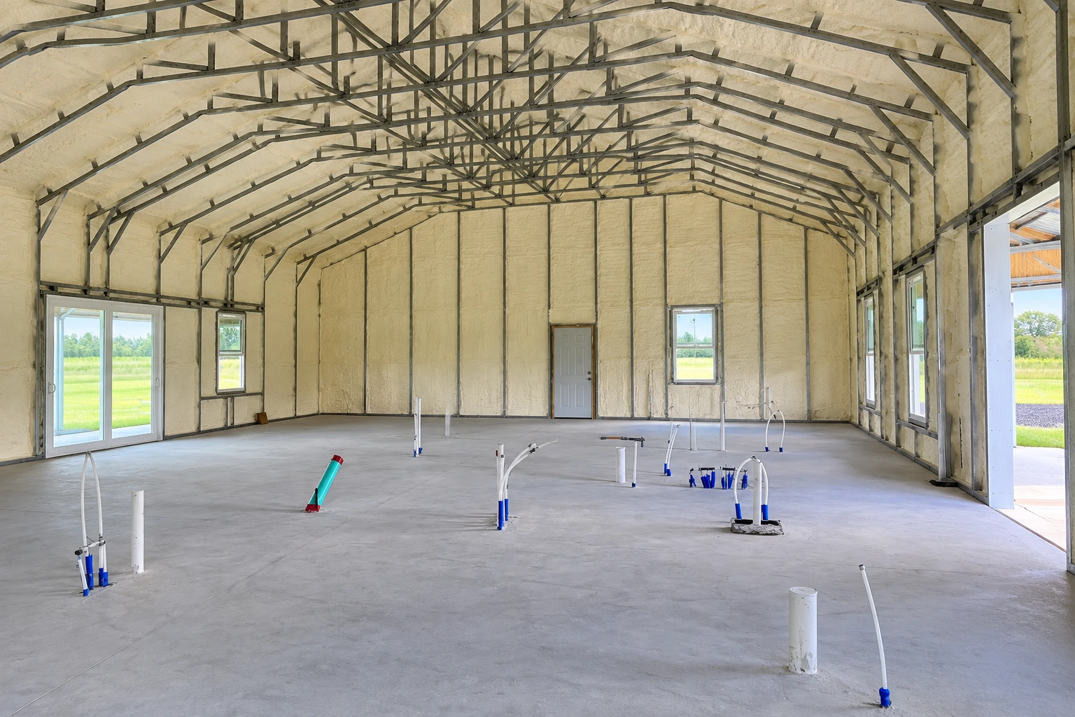 A large unfinished commercial building has cream-colored spray foam covering its walls and roof beneath exposed metal framing.